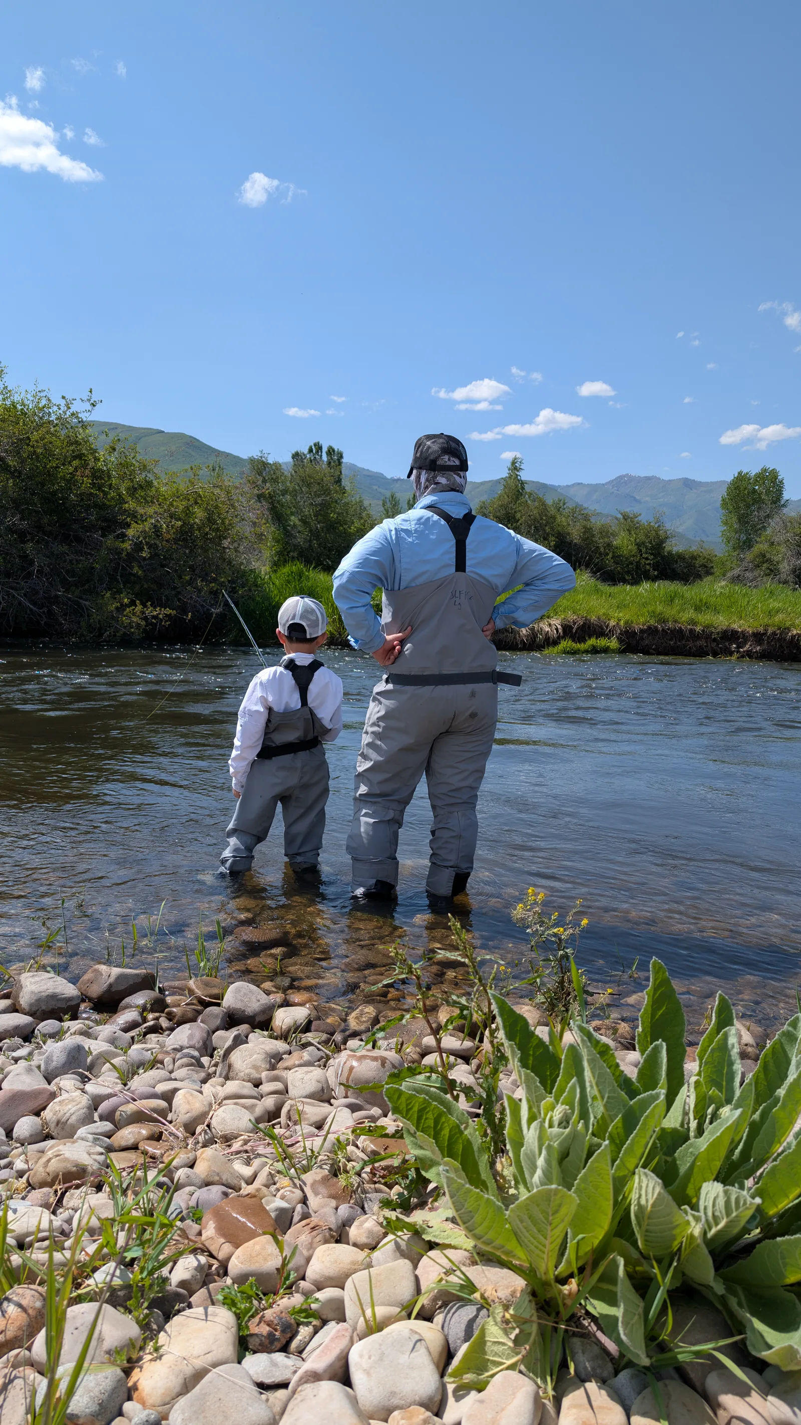 Dr. Baker and his son Isaac standing in a mountain river under a wide blue sky